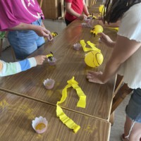 Kinder der Beet Buddies stehen an Holztischen und simulieren mit gelben Ballons, Förmchen und Blütenstaub spielerisch die Bestäubung durch Bienen.