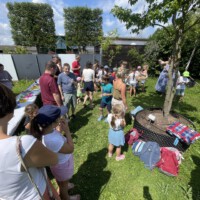 Familien und Kinder versammeln sich beim Sommerabschluss der Beet Buddies im Garten zu einem gemeinsamen Picknick an einem Buffet auf der sonnigen Wiese.